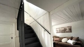 Una escalera conduce a una sala de estar con un sofá marrón y una obra de arte colgada en la pared.