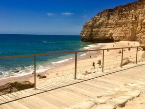 A beach with a wooden walkway leading to the shore, overlooking the ocean and a rocky cliff. - Apartment on the Beach in Vale Centianes (Lagoa)