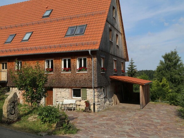 Stunning two-story house with a sloped roof and stone facade, surrounded by lush greenery.