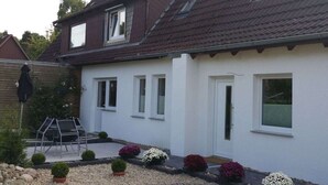 A two-story house with a white exterior, a tiled roof, and a small garden with various plants and a gravel pathway. - Holiday Apartment With a Terrace (Bremerhaven)