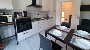 A modern kitchen with white cabinets, a black stove, and a microwave. There is a dining table with plates and cutlery. - Belvilla by OYO Sweet Lake D'orta (Omegna)