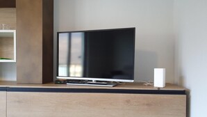 A flat-screen TV on a wooden cabinet with a remote control and a white device on the right. - Belvilla by OYO Sweet Lake D'orta (Omegna)