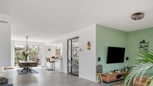 Un amplio espacio habitable con una mesa de comedor, sillas, un sofá y un televisor montado en la pared.