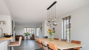 Un comedor moderno con una larga mesa de madera, seis sillas naranjas y un jarrón de flores.