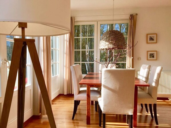 A dining area with a wooden table and chairs, large windows, and a hanging light fixture. - Holiday Home \"on the Beach\" (Zingst)