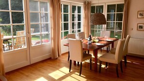 A dining room with a wooden table, six chairs, and a hanging light fixture. Large windows with curtains allow natural light to enter. - Holiday Home \"on the Beach\" (Zingst)
