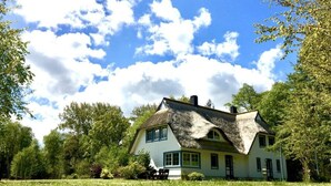 A traditional house with a thatched roof, surrounded by a lush green field and trees. - Holiday Home \"on the Beach\" (Zingst)