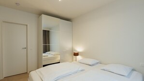Una habitación de hotel con cama, armario, espejo y mesita de noche con lámpara.