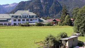 A large building with a green roof, surrounded by a grassy field and a mountain backdrop. - Lovely Apartment in Oberammergau (Oberammergau)