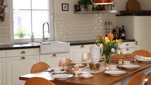 A kitchen with white cabinets, a copper pendant light, a window with a view of yellow flowers, and a dining table set with plates and cups.