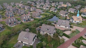 An aerial view of a residential area with houses, a small water body, and a road. - Villa Right by the sea (Julianadorp)