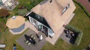 A modern house with a thatched roof, a patio with outdoor furniture, and a well-maintained garden. - Villa Right by the sea (Julianadorp)