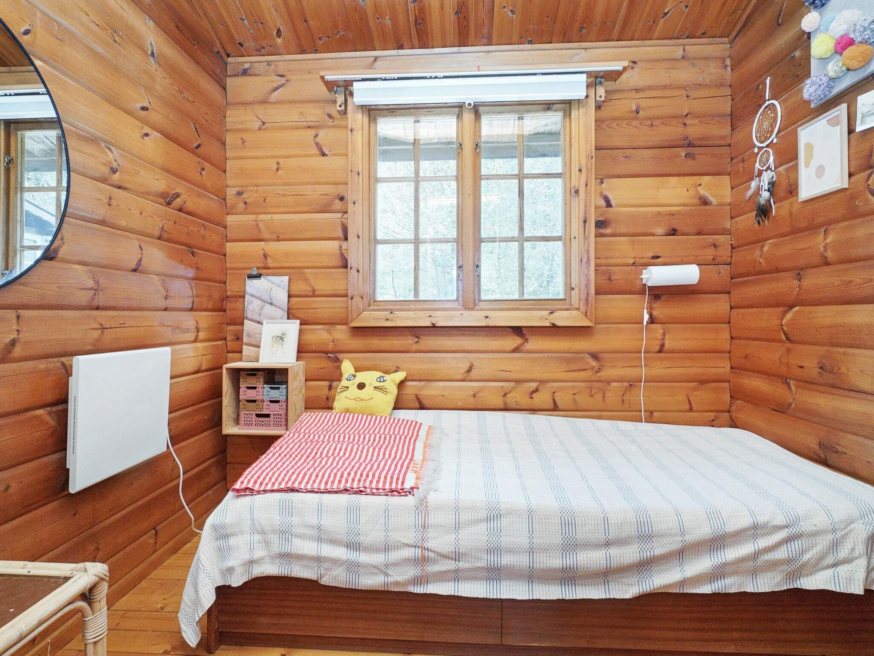 A cozy wooden cabin room with a bed, a window, a dreamcatcher, and a small table.