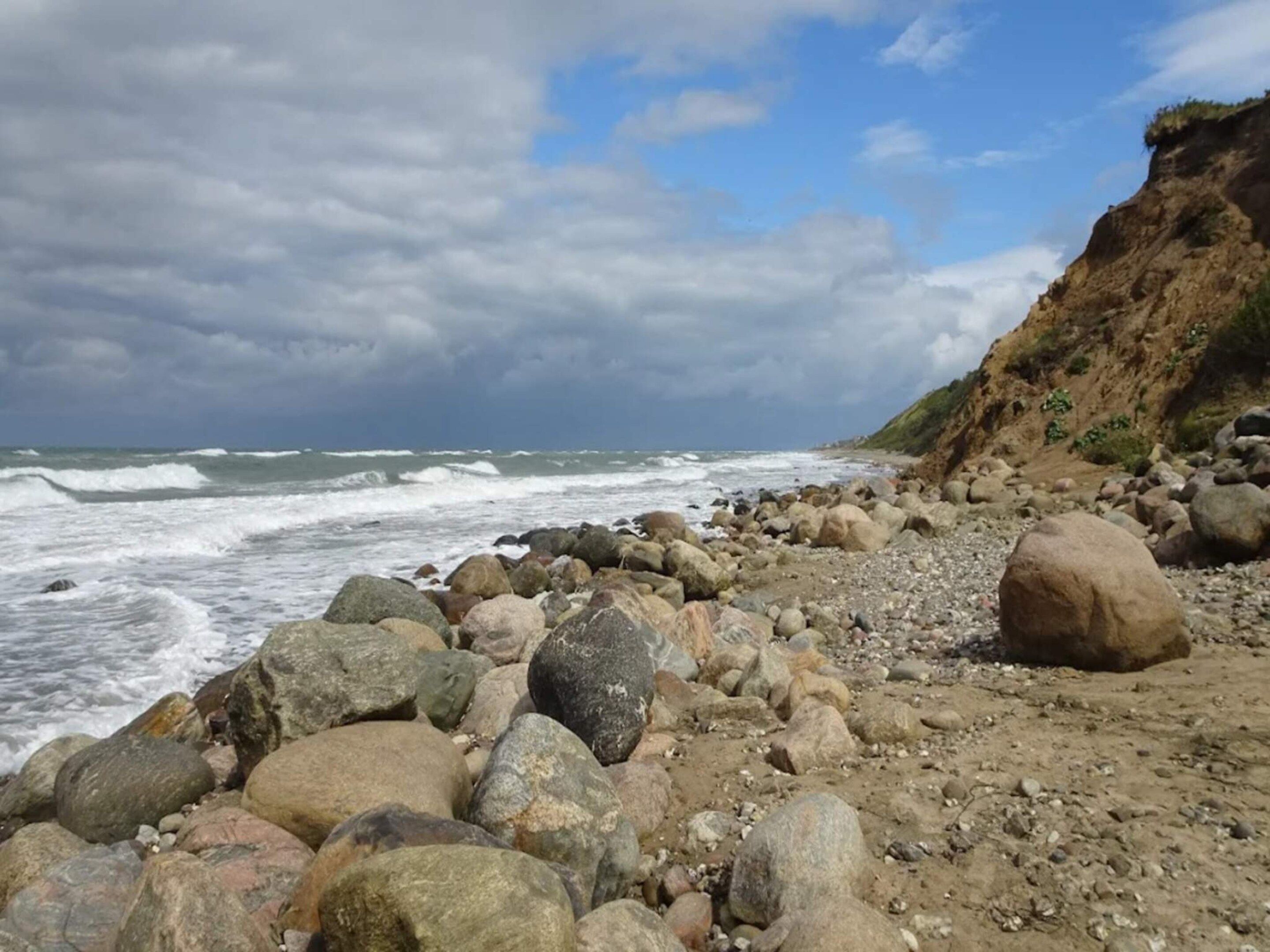 A rocky beach with waves crashing onto the shore and a cliff in the background.