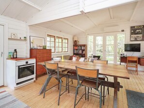 A spacious kitchen with a wooden table, chairs, and a built-in oven. There is a bookshelf and a television in the room.