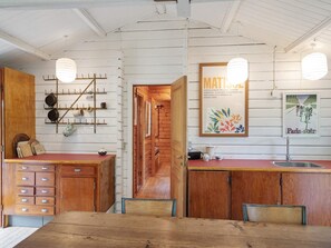 A rustic kitchen with wooden cabinets, a wooden dining table, hanging light fixtures, and a poster on the wall.