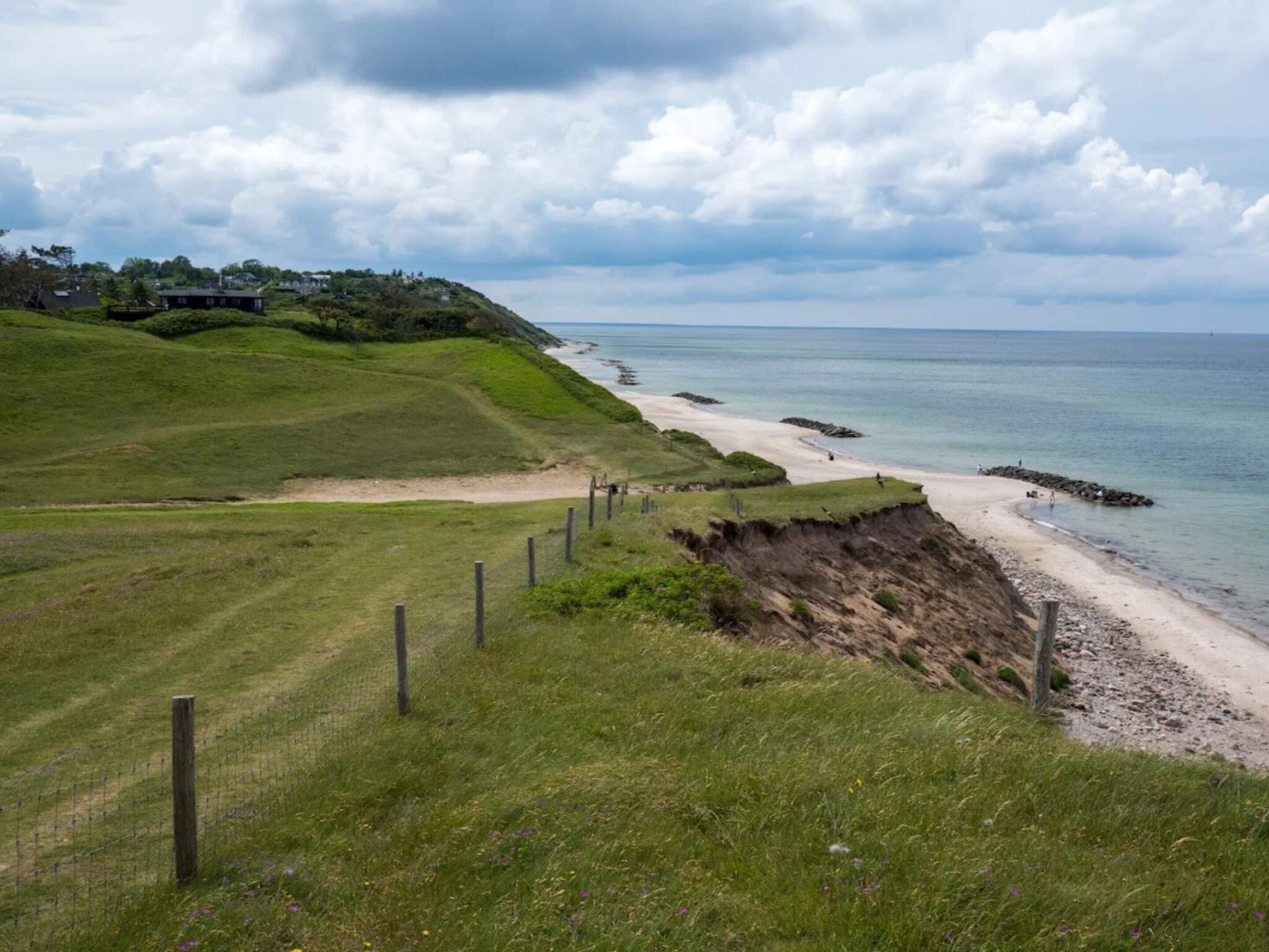 Un paysage côtier avec un sentier herbeux, une plage de sable et une étendue d’eau.