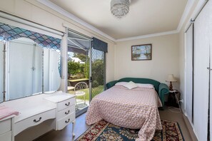Un dormitorio con cama, tocador, espejo, candelabro y vistas a través de un ventanal.