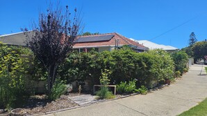 A residential house with a red-tiled roof, solar panels, and a well-maintained garden with various plants and flowers. - Albert Road Cottage: Comfy, vintage home near water & town  (East Bunbury)