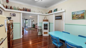 A dining area with a blue table and chairs, a guest pantry, and a collection of bottles on shelves. - Albert Road Cottage: Comfy, vintage home near water & town  (East Bunbury)