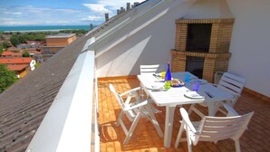 Eine Dachterrasse mit Backofen, weißem Tisch und Stühlen und Blick auf die Stadt.