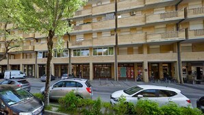 Ein mehrgeschossiges Gebäude mit Balkonen, geparkten Autos und einem Baum im Vordergrund.