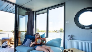 A room with a large window, a round window, a small stool, and a radiator. - Nice Houseboat in Kinrooi for Rent (Kinrooi)