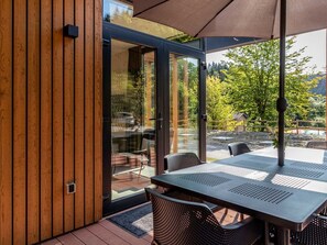 A modern outdoor dining area with a glass door leading to a patio, surrounded by wooden panels and a view of greenery. - Modern Holiday Home With hot tub in Winterberg (Winterberg)