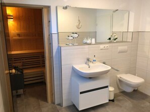 Une salle de bain moderne avec un sauna en bois, un lavabo blanc avec un miroir et des toilettes.
