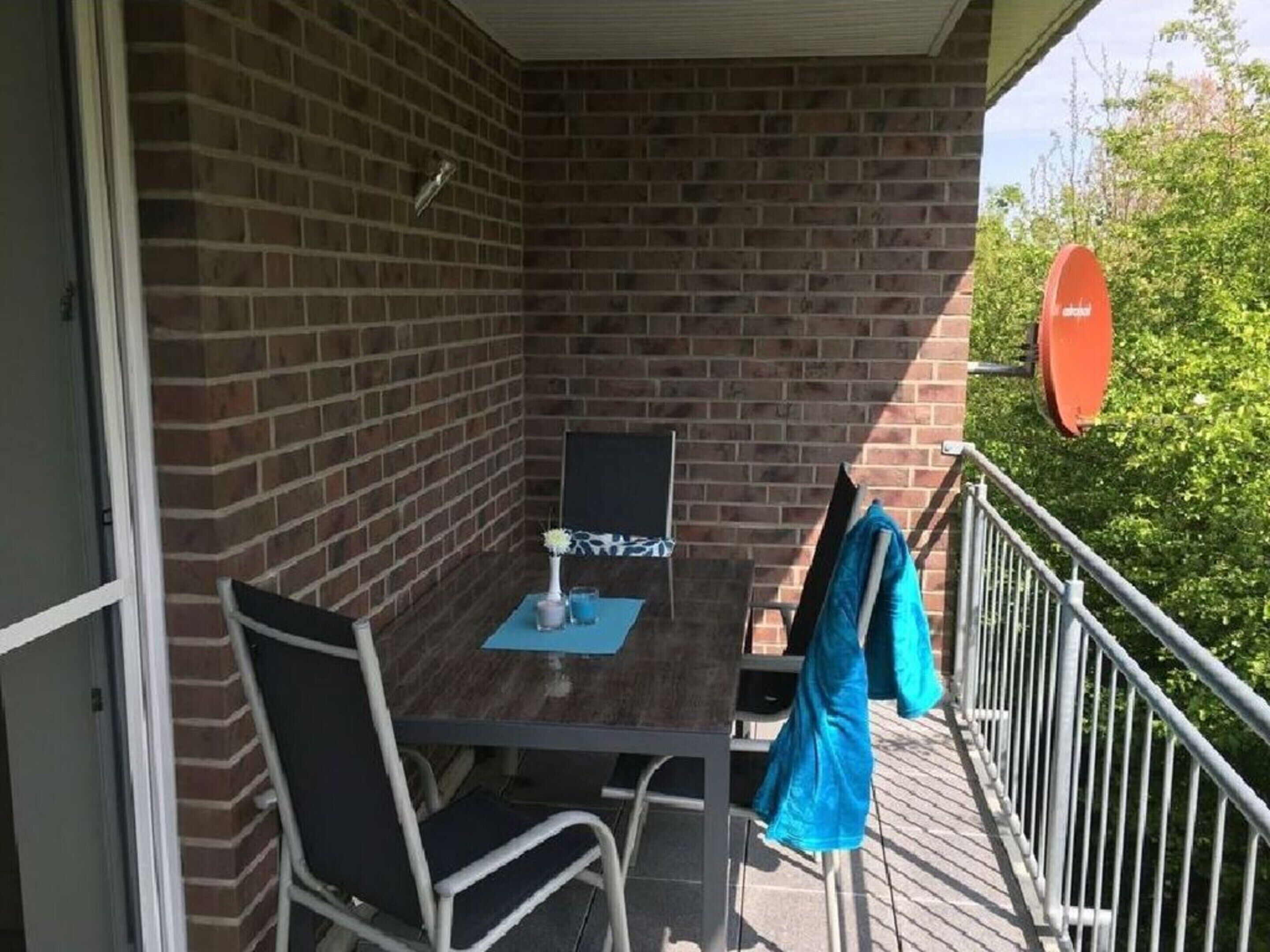 A balcony with a brick wall, a table with chairs, and a blue jacket hanging on the railing.