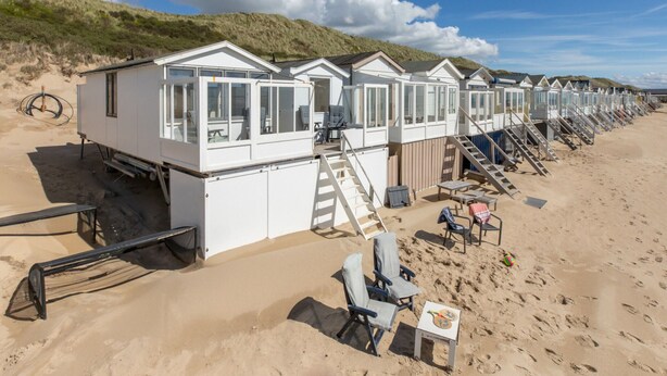 A row of beach huts with steps leading up to them, each with a small table and chair. - Holiday Home in Dishoek by the Beach (Koudekerke)