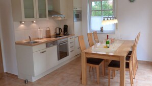 Une cuisine moderne avec des meubles blancs, un four encastré et un coin repas comprenant des chaises et une table en bois.
