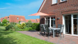 Une maison en briques dotée d’un patio comprenant une table et des chaises, un grand parasol et une porte-fenêtre coulissante.