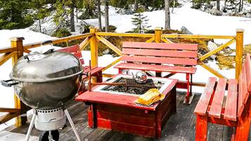 A wooden deck with a barbecue grill, a fire pit, and red benches.