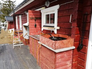 Een rood houten gebouw met een metalen wastafel, een raam en een klein buitengebied.