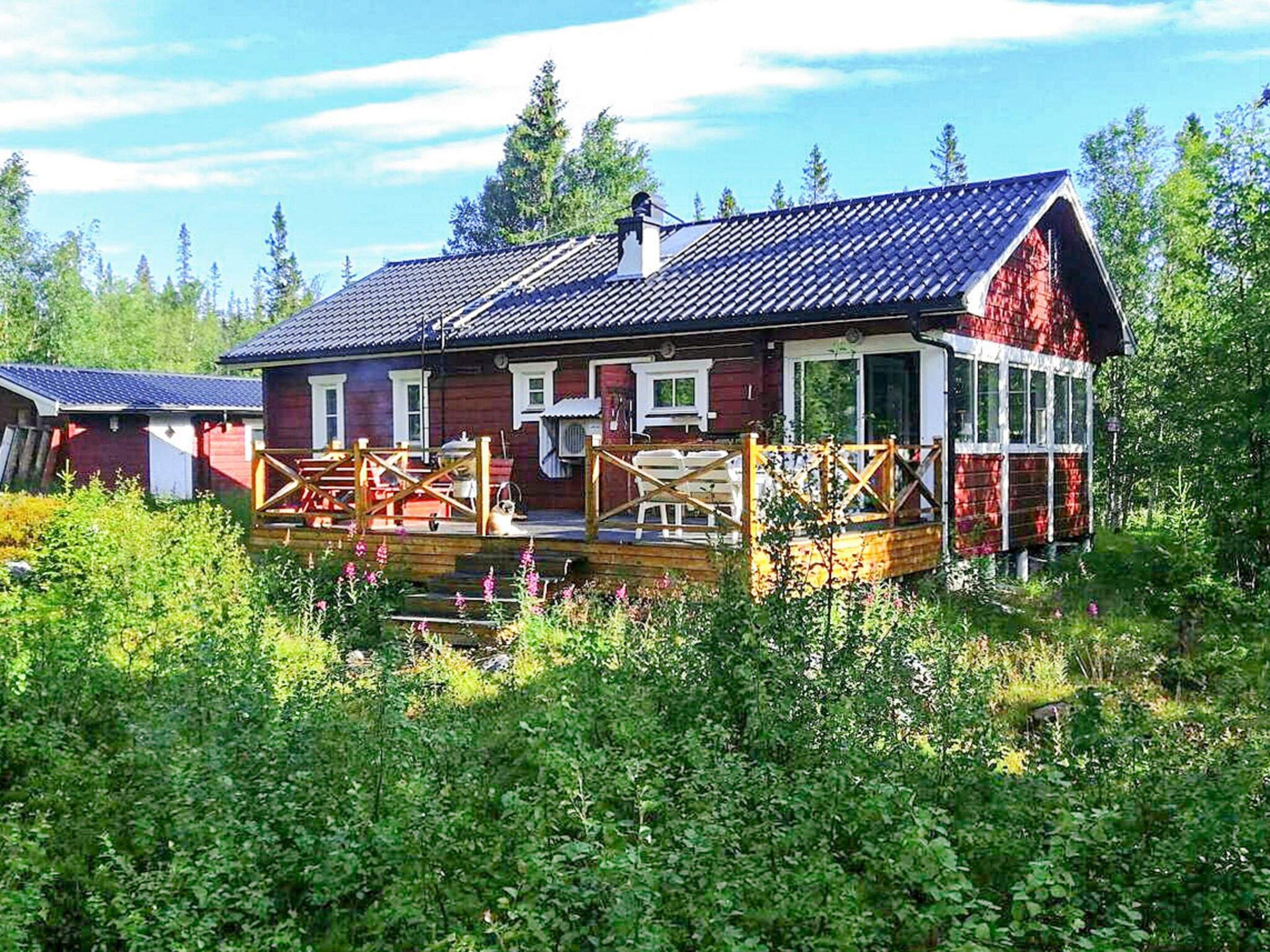 A red wooden house with a balcony, surrounded by greenery.