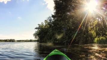 A green canoe on calm water with a forested shore and sunlight shining through the trees.