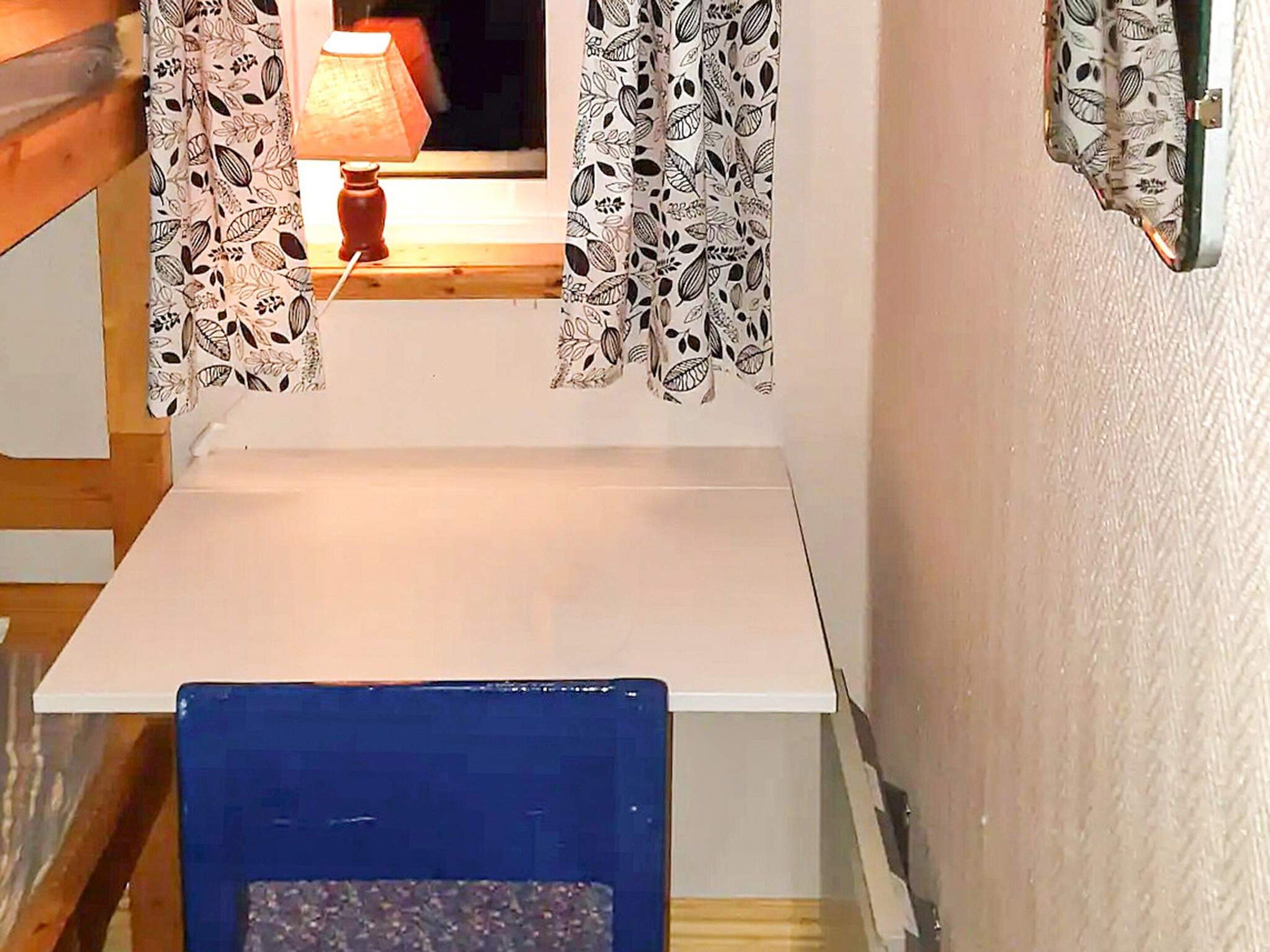 Ein Zimmer mit einem weißen Tisch, einem blauen Stuhl und gemusterten Vorhängen.