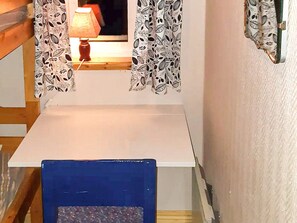 A room with a white table, a blue chair, patterned curtains, and a lamp. - 7 Person Holiday Home in Oviken (Oviken)