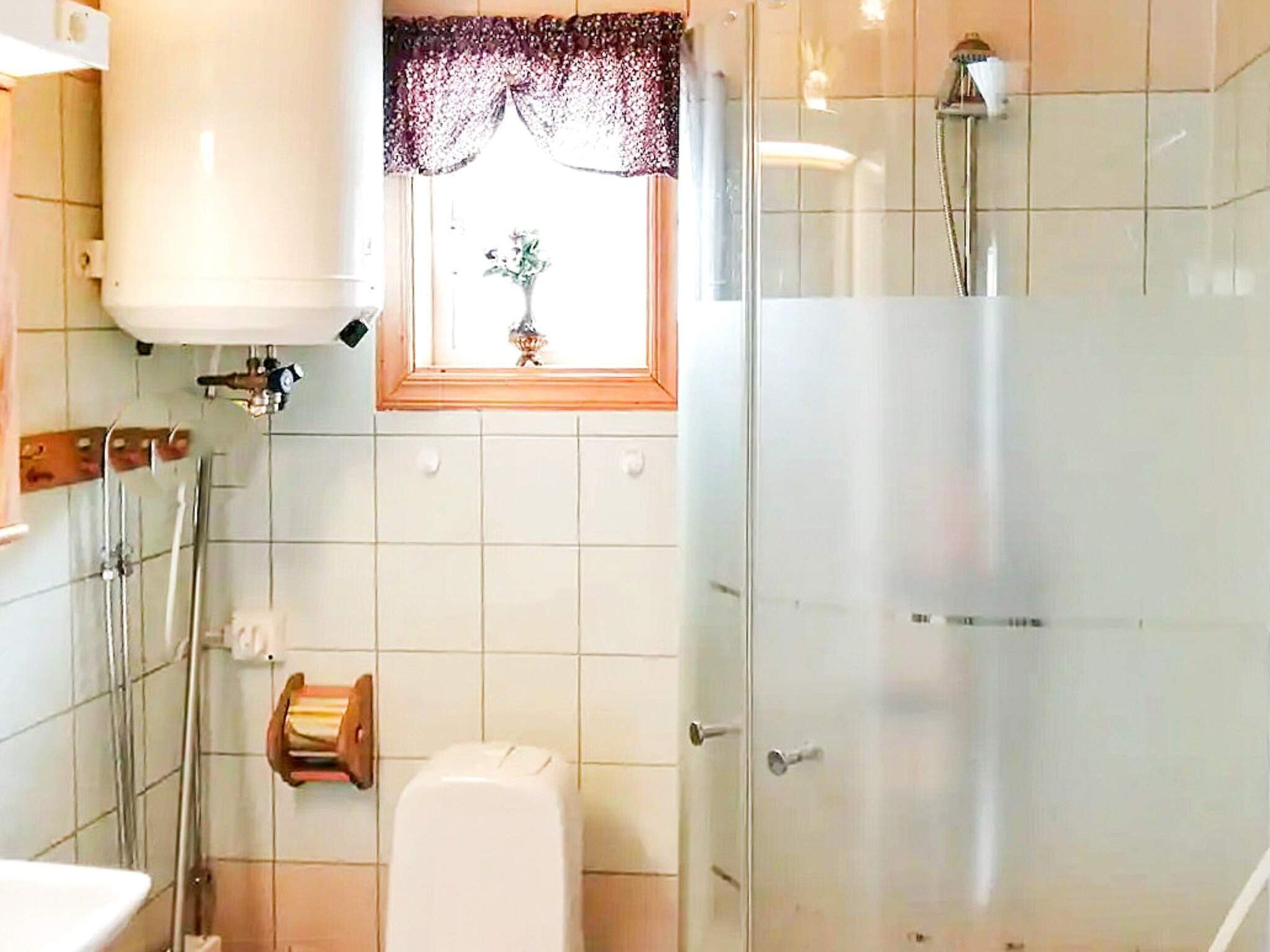 A bathroom with a toilet, a shower, and a window with a curtain.