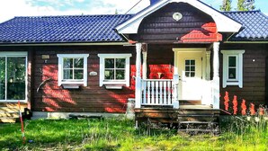 A wooden house with a porch, a chimney, and a small garden area.
