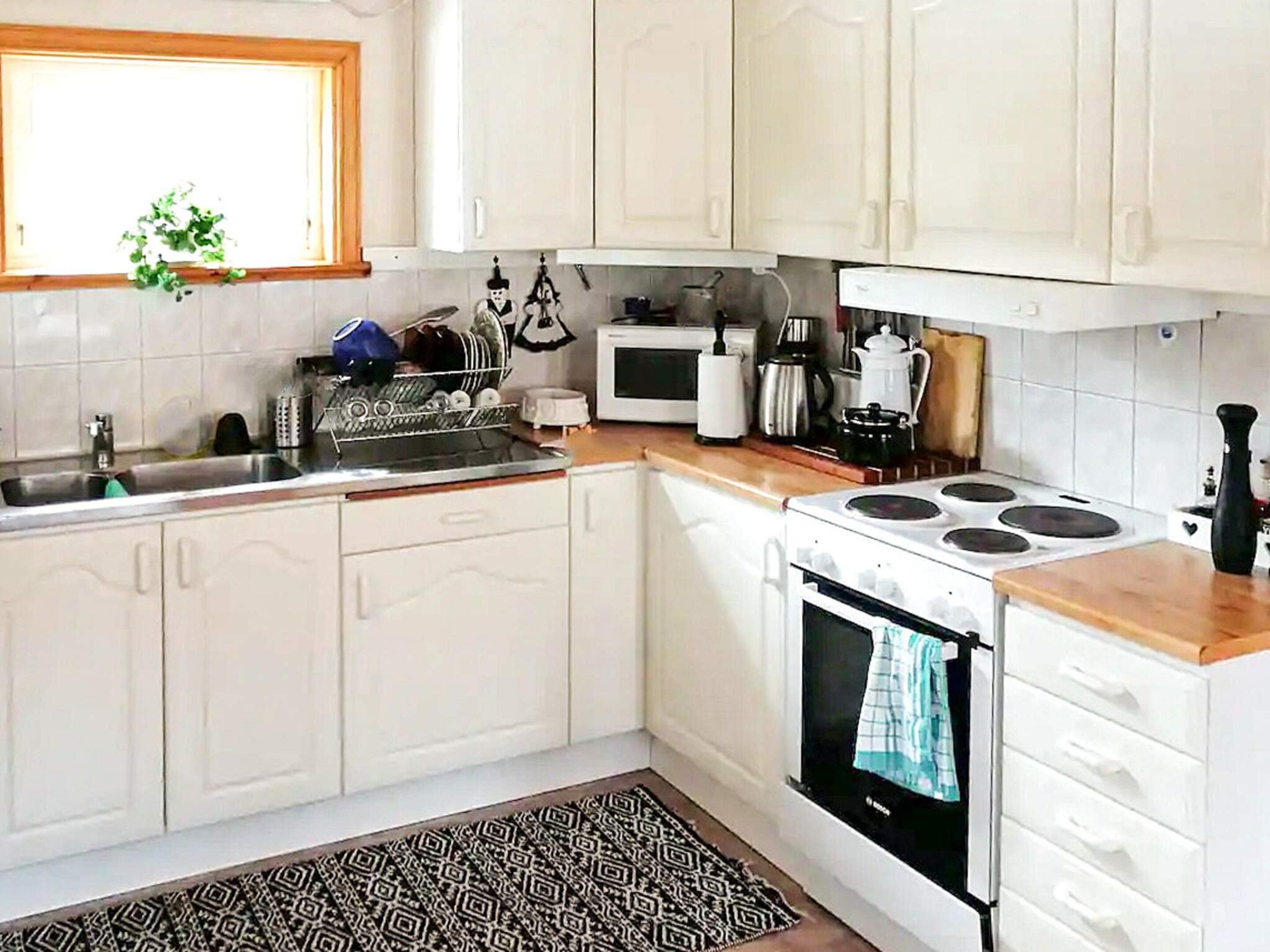 A kitchen with white cabinets, a stove, a microwave, and a sink.