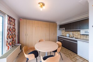 A modern kitchen with a round dining table, wooden cabinets, and a built-in microwave. - Cozy Studio on the 5th Floor With Terrace (Middelkerke)