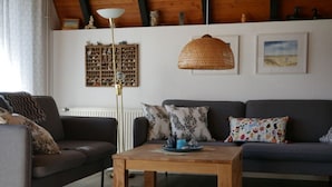 A living room with a sofa, a coffee table, a floor lamp, and a decorative wall shelf. - Long Comfortable Holiday Residence (Cuxhaven)