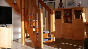 A wooden staircase with blue steps, a wooden cabinet with glass doors, and a television on a wooden stand. - Long Comfortable Holiday Residence (Cuxhaven)