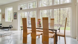 A dining area with a large table, six chairs, and a vase with flowers. - Forest Views, Enclosed Patio in Secluded Modern Home | Woodland Zen by AvantStay (Stockbridge)