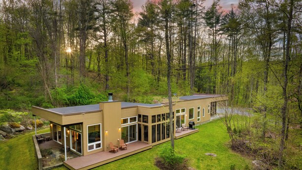 A modern house with a deck, large windows, and a view of the surrounding forest. - Forest Views, Enclosed Patio in Secluded Modern Home | Woodland Zen by AvantStay (Stockbridge)