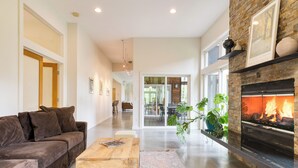 A modern living room with a fireplace, a sofa, a coffee table, and a large window. - Forest Views, Enclosed Patio in Secluded Modern Home | Woodland Zen by AvantStay (Stockbridge)