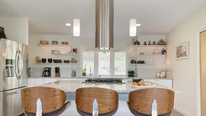 A modern kitchen with stainless steel appliances, wooden chairs, and a central island. - Forest Views, Enclosed Patio in Secluded Modern Home | Woodland Zen by AvantStay (Stockbridge)