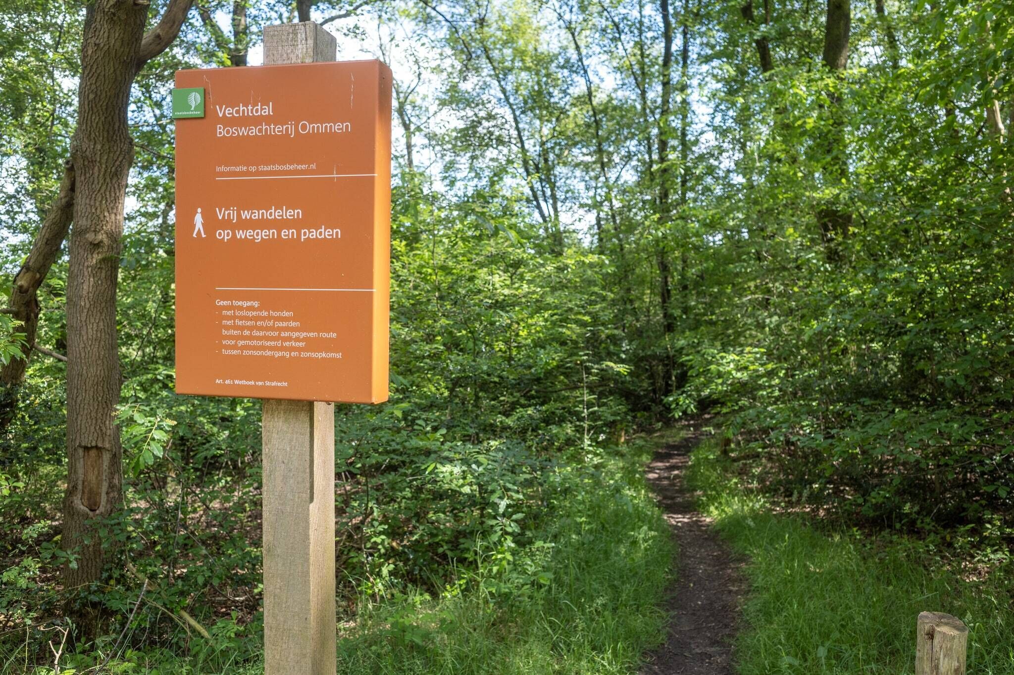 A sign in a wooded area with a path, indicating it is a walking and cycling route.